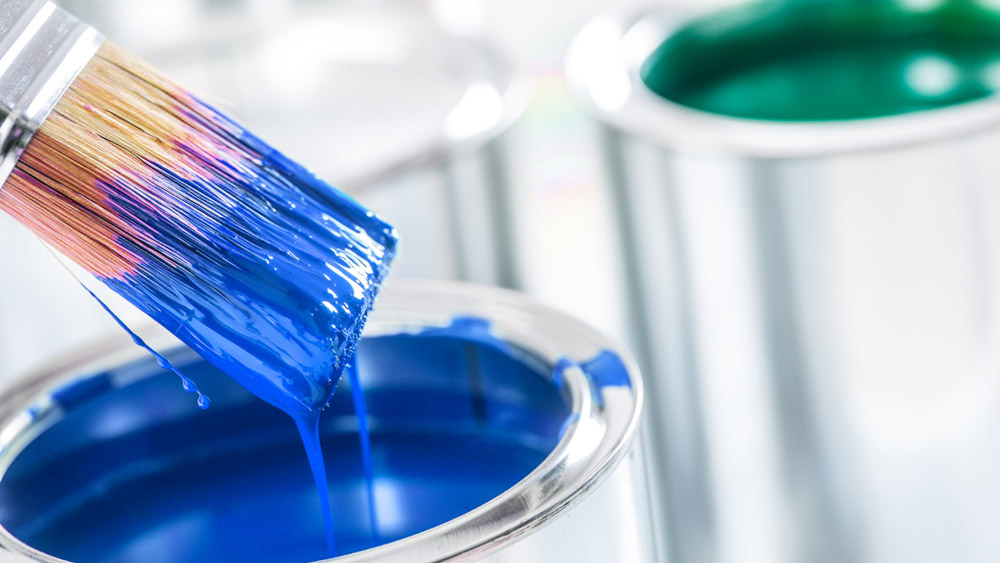 Zwei Farbeimer mit blauer und grüner Farbe sowie ein tropfender Pinsel – Wissen Sie, welche Schadstoffe in Farben & Co. stecken?